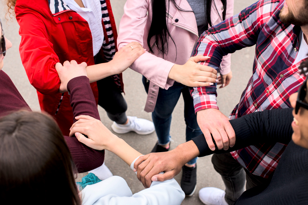 Elevated view of diverse friends holding each other’s hands on the street, illustrating the concept of social prescribing for students and community-based mental health support. This image represents peer navigators in mental health helping each other, showcasing student mental health support and improving student well-being. It highlights the benefits of social prescribing in fostering connections and support.